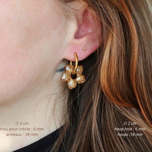 K&ouml;nnte beinhalten: Ein goldfarbener Creolen-Ohrring mit einem f&uuml;nfbl&auml;ttrigen Blumenanh&auml;nger in glitzernder, texturierter Optik. Der Ohrring hat einen Durchmesser von 2 cm, ein 6 mm gro&szlig;es Loch und 18 mm gro&szlig;e Ringe, wobei der Text diese Ma&szlig;e deutlich angibt.
