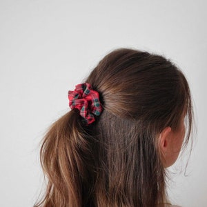May include: A red, green, and white plaid scrunchie is tied in a low ponytail. The hair accessory is made of a soft fabric and adds a pop of color to the hairstyle. The scrunchie is a classic hair accessory.