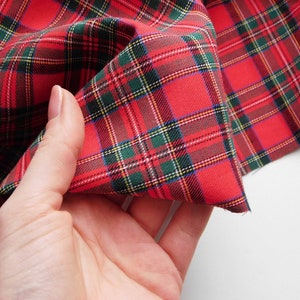 May include: Close-up of red plaid fabric with green, yellow, and white accents. The fabric is folded, showcasing the pattern's detail. This textile is suitable for various crafting and sewing projects.