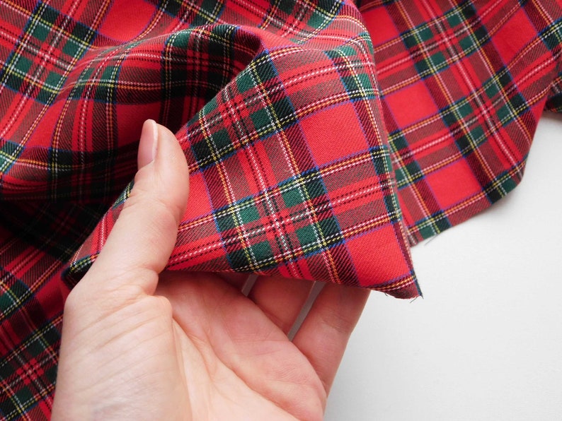 May include: Close-up of red plaid fabric with green, yellow, and white accents. The fabric is folded, showcasing the pattern's detail. This textile is suitable for various crafting and sewing projects.