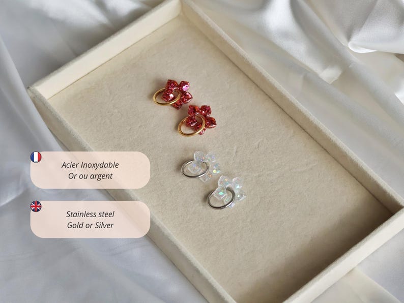 K&ouml;nnte beinhalten: Zwei Paar Creolen mit blumenf&ouml;rmigen Anh&auml;ngern. Ein Paar hat rote Glitzerblumen an goldfarbenen Ringen, das andere Paar hat irisierende wei&szlig;e Blumen an silberfarbenen Ringen. Der Text auf dem Bild lautet Acier Inoxydable Or ou argent und Stainless steel Gold or Silver.