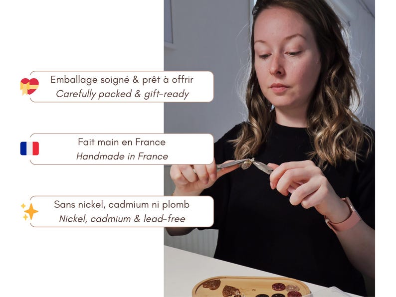 K&ouml;nnte beinhalten: Eine Metallzange wird verwendet, um einen kleinen Metallanh&auml;nger zusammenzusetzen. Drei Textfelder sind sichtbar: Emballage soign&eacute; & pr&ecirc;t &agrave; offrir, Fait main en France und Sans nickel, cadmium ni plomb, jeweils mit englischer &Uuml;bersetzung.