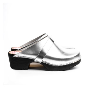 May include: Silver leather clogs with a black wooden heel and a black sole.