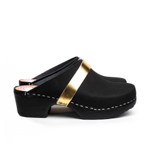 May include: Black leather clogs with a gold band across the top of the foot. The clogs have a wooden heel and a white stitch detail around the edge.