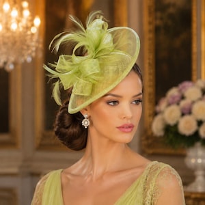 May include: A lime green fascinator hat featuring a wide, circular sinamay base adorned with structured loops of matching fabric and delicate, wispy feathers. The headpiece is worn at an angle, showcasing a textured weave and a vibrant, monochromatic colour palette.