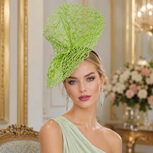 Peut inclure: Un bibi vert citron vif doté d'une structure complexe en maille ouverte, semblable à une toile, qui s'élève verticalement. L'accessoire est fixé sur un serre-tête noir fin, présentant un design sculptural abstrait à la finition fibreuse.