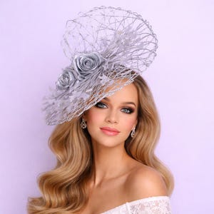 Peut inclure: Coiffe argentée avec un délicat motif en filet, ornée de roses argentées et de plumes. Ce chapeau de cérémonie est un accessoire élégant pour les occasions spéciales, comme les mariages.