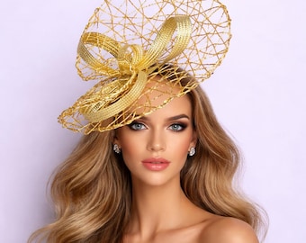 May include: A gold-colored headpiece with a bow and netting design. The headpiece is made of woven material and is worn on the head. The headpiece is a formal accessory, suitable for special occasions.
