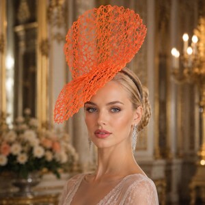 Peut inclure: Un fascinateur orange vif doté d'une structure complexe en maille ouverte, semblable à une toile, qui s'élève verticalement depuis un serre-tête fin. La coiffe présente un grand design circulaire en éventail avec un motif en treillis texturé.