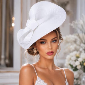 May include: A white wide-brimmed hat featuring a large, structured bow detail on the side. The hat is constructed from a woven material with a smooth, uniform texture and a clean, bright white finish, designed to sit at an angle on the head.