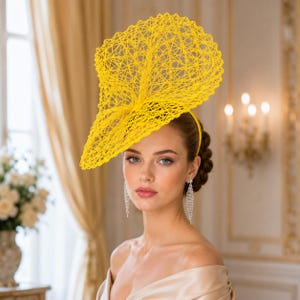 Könnte beinhalten: Ein leuchtend gelber Fascinator mit einer komplexen, netzartigen Gitterstruktur. Das Kopfstück ist auf einem dünnen Haarreifen befestigt und zeigt ein großes, skulpturales, fächerförmiges Design mit einem feinen, durchbrochenen Muster.