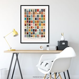 May include: A framed poster with a colorful design of book covers. The poster is titled "The Library of a Lifetime". The poster is hanging on a white wall above a desk with a lamp, a chair, and other office supplies.