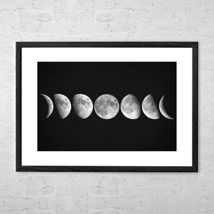 Puede incluir: Impresión enmarcada en blanco y negro de las fases lunares. La imagen muestra la luna en diferentes fases, desde la creciente hasta la llena, sobre un fondo negro. La impresión está en un marco negro.