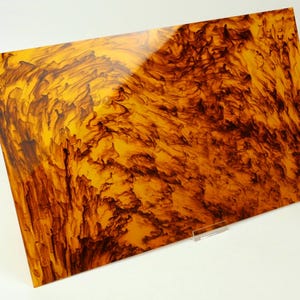 May include: A rectangular sheet with a glossy finish featuring a marbled pattern of deep amber and dark brown swirls. The surface displays a high-contrast, organic design with translucent golden-yellow areas blended with dark, intricate streaks.