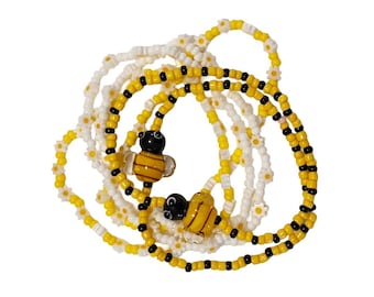 Può includere: Una collezione di gioielli di perline a tema ape. I fili combinano perline bianche a forma di margherita, perline gialle e nere e ciondoli a forma di ape in vetro. Le perline sono infilate insieme per creare un design giocoso e stravagante.