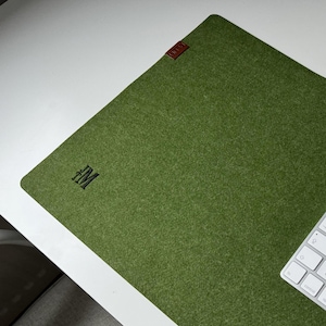 Pode incluir: Um tapete de mesa de feltro verde com um teclado sem fio branco e as letras "FM" no canto superior esquerdo.