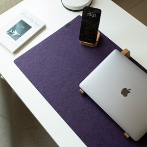 Puede incluir: Una alfombrilla de escritorio de fieltro morado con un ordenador portátil en un soporte de madera, un teléfono inteligente y un libro con el texto "do it for her".