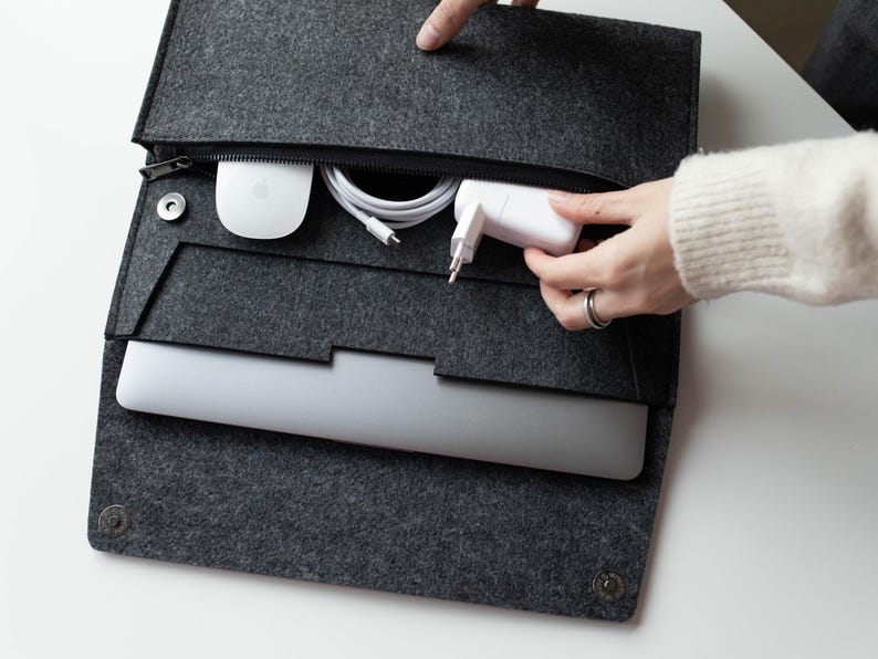 May include: A gray felt laptop sleeve with a zipper closure. The sleeve is open and contains a laptop, a white charging brick, a white wireless mouse, and a white charging cable.