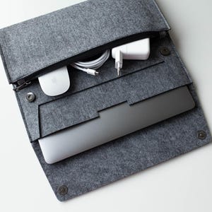 May include: A gray felt laptop sleeve with a zipper closure. The sleeve is open and contains a laptop, a white power adapter, a white wireless mouse, and a white charging cable.