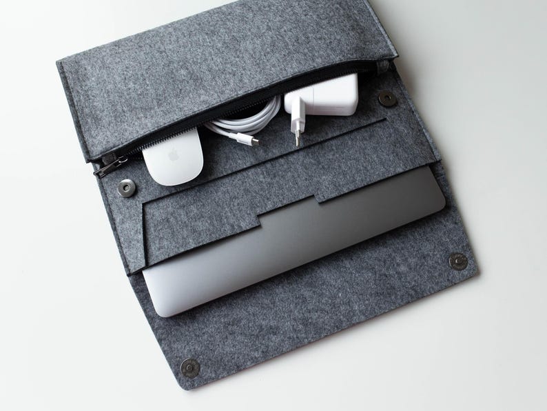 May include: A gray felt laptop sleeve with a zipper closure. The sleeve is open and contains a laptop, a white power adapter, a white wireless mouse, and a white charging cable.