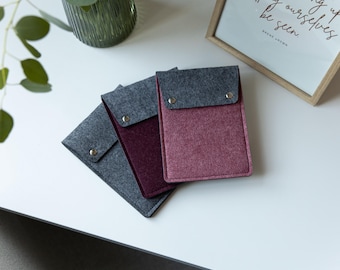 May include: Three rectangular felt sleeves with fold-over flaps secured by silver-toned metal snaps. The sleeves feature a dark grey flap and bodies in varying shades of grey, deep burgundy, and dusty rose, arranged in a layered, overlapping stack.