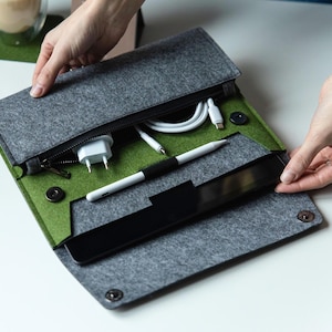 May include: A grey felt envelope-style organizer case with a green interior lining. The case features a zippered compartment containing a white power adapter and charging cable, along with a white stylus and a black tablet device inside.