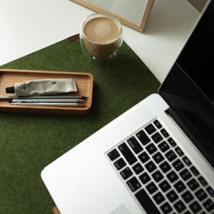 May include: A green felt desk mat with a wooden tray containing a tube of cream, pencils, and a cup of coffee on a white surface.