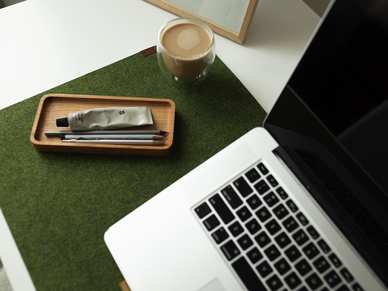 May include: A green felt desk mat with a wooden tray containing a tube of cream, pencils, and a cup of coffee on a white surface.