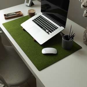 May include: A green felt desk mat with a laptop computer, a wireless mouse, and a pencil holder with pencils on a white desk.