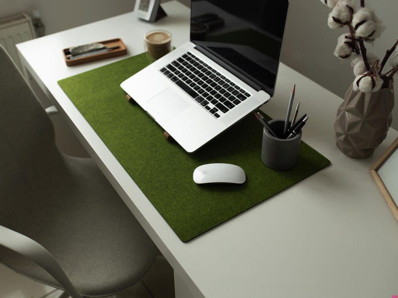 May include: A green felt desk mat with a laptop computer, a wireless mouse, and a pencil holder with pencils on a white desk.