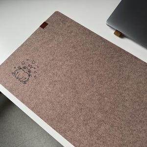 May include: A brown felt mouse pad with a black outline of a frog wearing a crown and surrounded by hearts.
