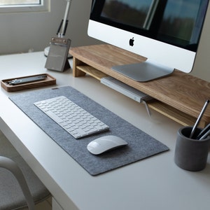 Peut inclure: Un clavier d'ordinateur blanc et une souris sur un tapis de bureau en feutre gris. Le clavier est sur un bureau blanc avec un support d'écran en bois et un porte-crayons gris.