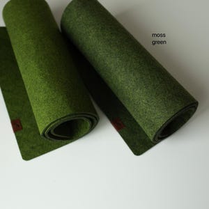 May include: Two rolled-up felt placemats in olive green and moss green. The placemats are rolled up and have a brown leather tag on the end.