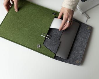 Könnte beinhalten: Eine zweifarbige Laptop-Hülle aus Filz mit einer olivgrünen Außenklappe und einem anthrazitfarbenen Innenfach. Die Hülle verfügt über zwei Stiftschlaufen aus silberfarbenem Metall, einen Magnetverschluss und ein Fach für einen flachen Laptop.