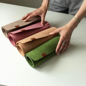 May include: Four rolled-up felt placemats in different colors: beige, pink, brown, and green. Each placemat has a brown leather label.