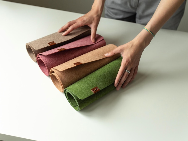 May include: Four rolled-up felt placemats in different colors: beige, pink, brown, and green. Each placemat has a brown leather label.
