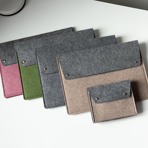 May include: A collection of five rectangular felt pouches with fold-over flaps secured by silver-toned metal snaps. The pouches feature a dark gray felt flap paired with bodies in pink, green, dark gray, beige, and a smaller beige version.
