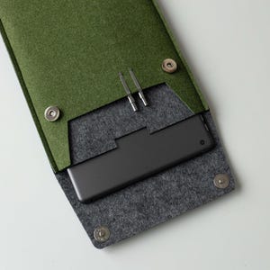 以下が含まれることがあります： 緑色のフェルトケース。グレーの内部に黒い長方形のデバイスと2つの銀色のツールが入っています。ケースは3つの銀色のスナップ留めで固定されています。デバイスには小さな円形のディテールがあります。