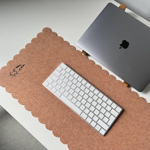 Puede incluir: Una configuraci&oacute;n de espacio de trabajo con un port&aacute;til gris, un teclado blanco y una alfombrilla de escritorio con borde festoneado de color marr&oacute;n rojizo. La alfombrilla tiene un dise&ntilde;o floral. Los elementos est&aacute;n sobre un escritorio blanco.