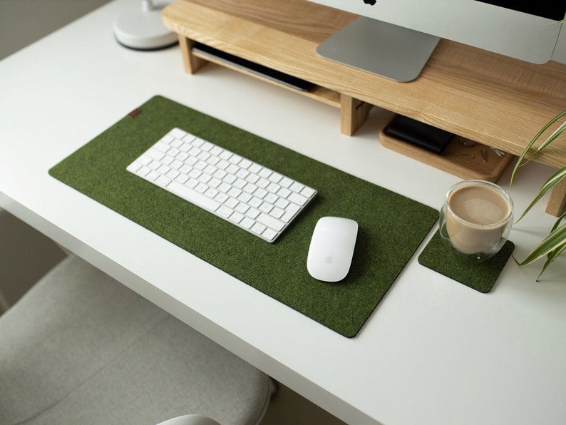 May include: A green felt desk mat with a white keyboard and a white mouse. A glass mug with a brown beverage sits on a green felt coaster.