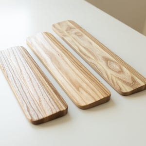 May include: Three rectangular wooden boards with rounded corners, each featuring a distinct light brown wood grain pattern. The boards are arranged diagonally, showcasing the natural texture and variations in the wood's light and dark tones.