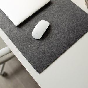 May include: A white wireless mouse on a gray felt desk mat. The mat is on a white desk.