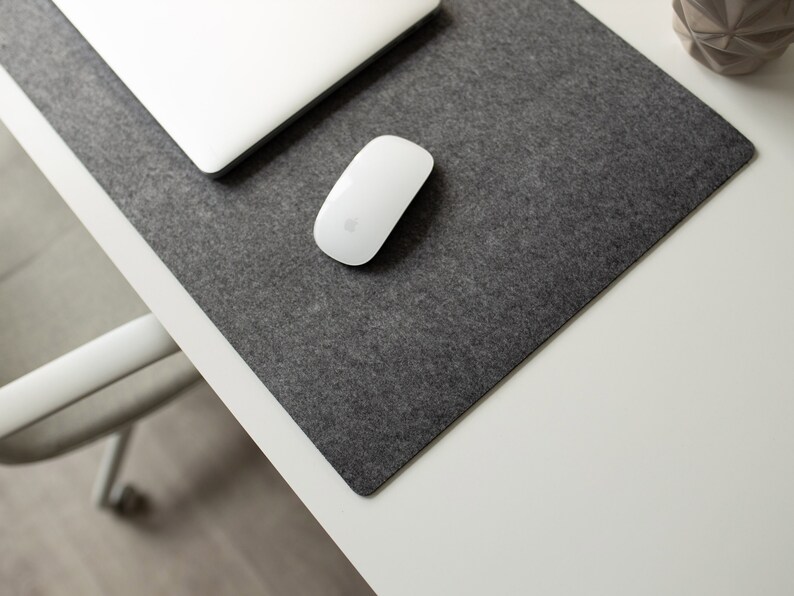 May include: A white wireless mouse on a gray felt desk mat. The mat is on a white desk.