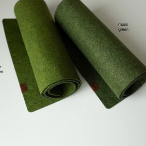 May include: Two felt placemats in different shades of green. The placemat on the left is olive green and the placemat on the right is moss green.