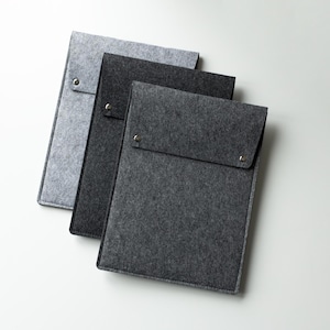 Peut inclure: Trois pochettes rectangulaires en feutre pour appareils électroniques ou documents, disposées en pile superposée. Chaque pochette présente un rabat repliable fixé par un bouton-pression métallique. Les couleurs varient du gris clair au gris anthracite.