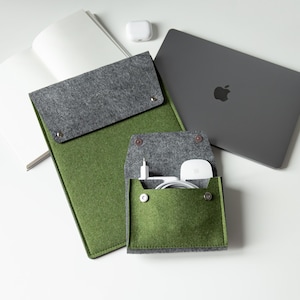 May include: A green felt laptop sleeve and accessory pouch with a gray flap, next to a gray laptop with an Apple logo. A white notepad, earbuds, and charging accessories are also visible.