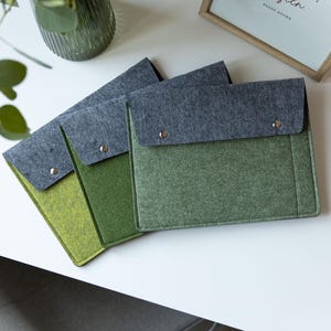 May include: Three rectangular felt document sleeves with fold-over flaps secured by silver-toned metal snaps. Each sleeve features a dark charcoal grey flap and a body in varying shades of green, ranging from light lime to deep olive green.
