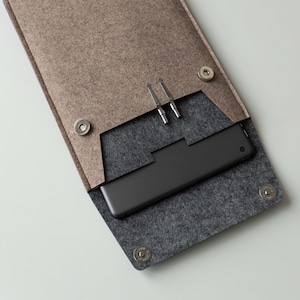 May include: A brown felt case with a black felt lining and a zipper closure. A tablet computer is inside the case, along with two metal styluses.