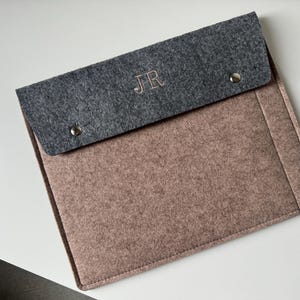 May include: A rectangular felt laptop sleeve featuring a light brown main body and a dark gray fold-over flap. The flap is secured with two silver-toned metal snap buttons and displays the embroidered initials JR in a light-colored thread.