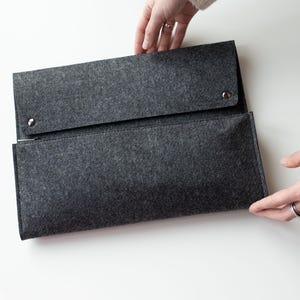 May include: A gray felt zippered pouch with a flap closure and two silver snaps. The pouch is open and being held by a hand.